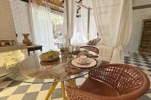 Una habitación con una mesa de vidrio, sillas de mimbre, un sofá blanco y un suelo a cuadros.