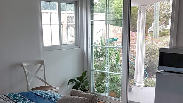 A bedroom with a bed, a chair, a TV, and a sliding glass door leading to an outdoor area. - Coastal Grevillea Studio Retreat ,a place to relax or enjoy the outdoors (Ettalong Beach)