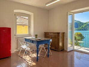 Ein Zimmer mit Tisch, Stühlen, einem roten Kühlschrank, einem Fenster mit Bergblick und einem Balkon mit einem Sessel.