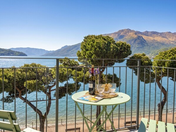 Ein Balkon mit Tisch, einer Flasche und Gläsern mit Blick auf einen See und Berge.