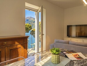 Ein Zimmer mit einem Holzkasten, einem Marmortisch mit Topfpflanze, einem grauen Sofa und einem Fernseher auf einem Schrank.