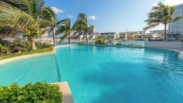 A swimming pool surrounded by palm trees and hotel buildings. - Cancun 2BR: Resort Pool, Padel & Playground (Cancún)
