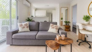 A modern living room with a grey sofa, a small round table, and a white desk with a chair. - Broadbeach | 2Min to Beach | Pool | Free Parking (Broadbeach)