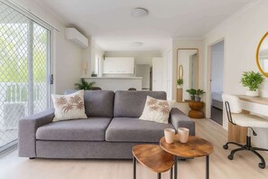 Ein modernes Wohnzimmer mit einem grauen Sofa, einem kleinen runden Tisch und einem weißen Schreibtisch mit einem Stuhl.