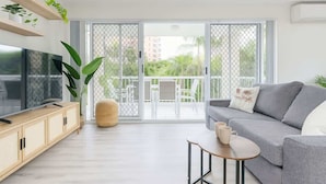 A modern living room with a sofa, TV, and a small table. - Broadbeach | 2Min to Beach | Pool | Free Parking (Broadbeach)