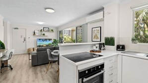 A modern kitchen with white cabinets, a built-in oven, and a dining area with a grey sofa and chairs. - Broadbeach | 2Min to Beach | Pool | Free Parking (Broadbeach)