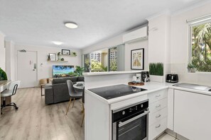 Eine moderne Küche mit weißen Schränken, einem eingebauten Backofen und einer Essecke mit grauem Sofa und Stühlen.