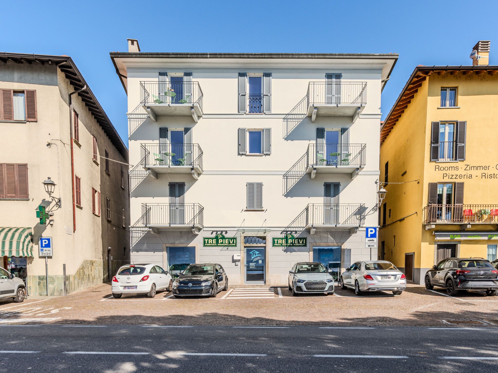A multi-story building with a central entrance, parking spaces, and a sign for 'TRE PIEVEI'.