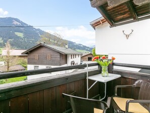 A balcony with a view of a mountain landscape, a wooden table with a vase of flowers, and a deer skull mounted on the wall. - Cozy holiday apartment in Westendorf (Westendorf)