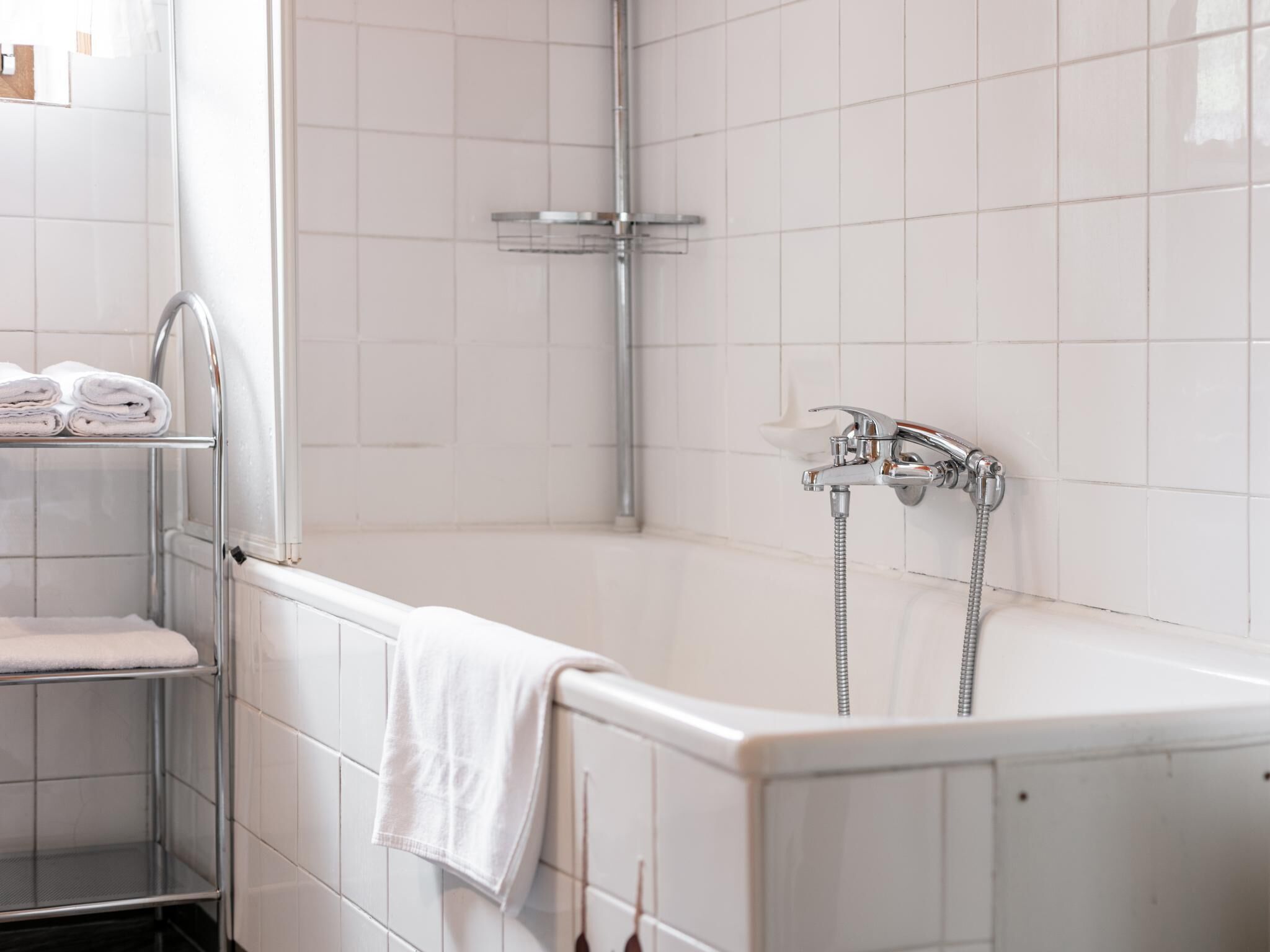 Un bagno con vasca, doccia e porta asciugamani con asciugni piegati.