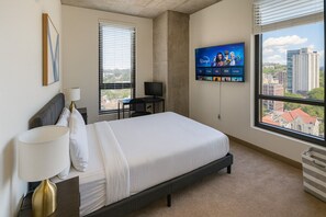 A hotel room with a bed, a desk, a TV, and a window with a city view. - Five Points South | Spacious 2BR w/ 2 Queens D5 (Birmingham)