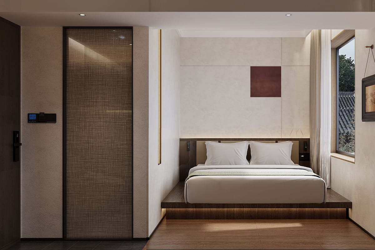A modern hotel room with a bed, a digital clock, a window, and a view of the outside.