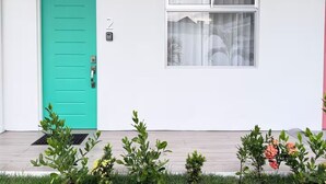 Eine türkisblaue Tür, ein Schild mit der Nummer 2, ein Fenster mit Vorhängen und ein kleiner Garten mit Pflanzen und Blumen.