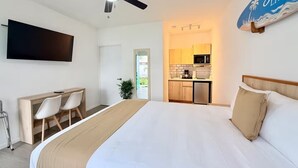 Ein Hotelzimmer mit Bett, Schreibtisch, Stuhl, Fernseher, Deckenventilator und einer Küchenzeile.