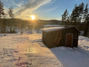 A wooden cabin in a snowy landscape with a clear sky and sun.