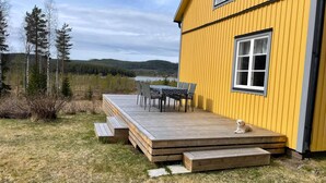 A yellow building with a deck, outdoor seating, and a view of a lake and forest. - Beautiful peaceful house! (Rätan)