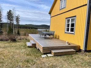 A yellow building with a deck, outdoor seating, and a view of a lake and forest.