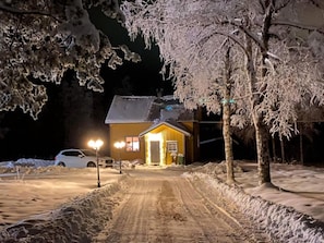 A snow-covered landscape with a cabin, a dirt road, and a parked car.