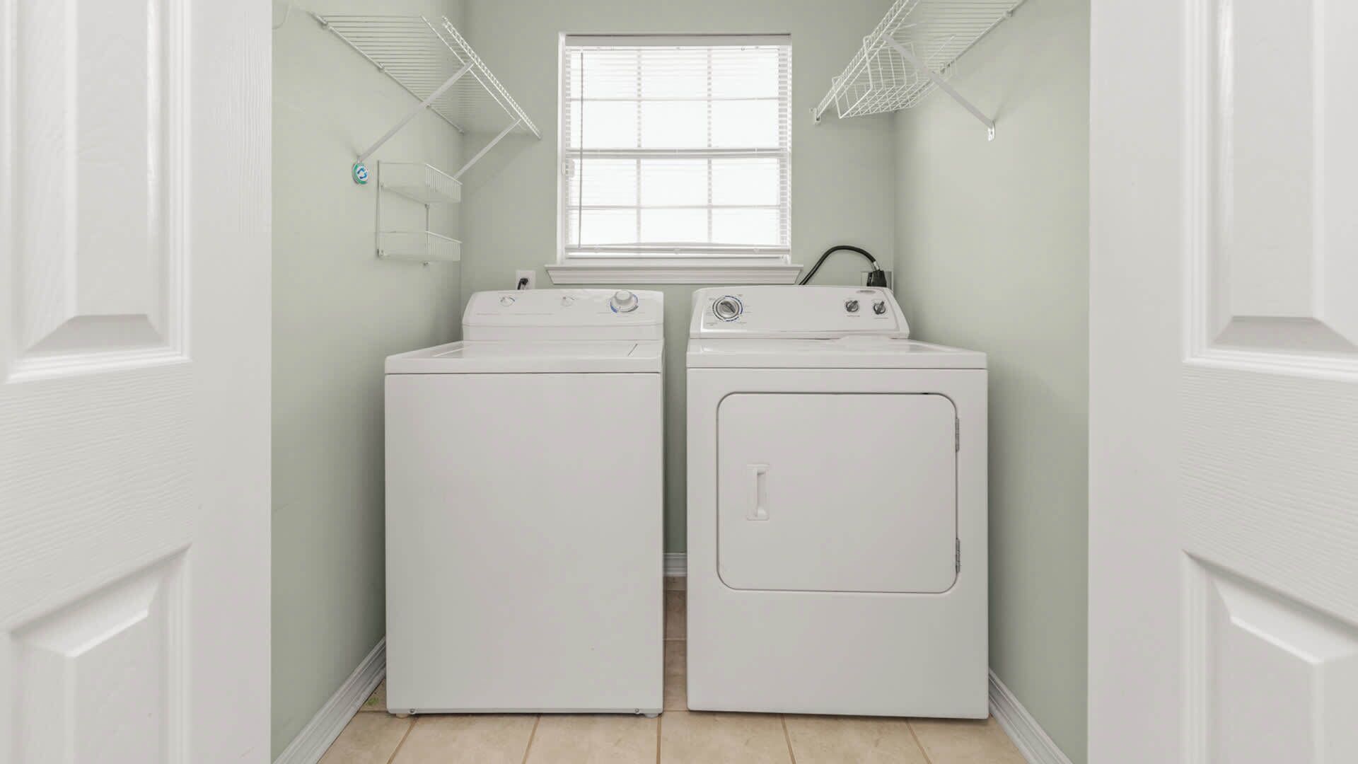 Une buanderie avec deux machines à laver et deux sèche-linge blancs, une fenêtre et une porte blanche.
