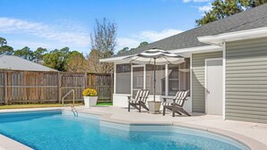 Ein Schwimmbad mit überdachter Terrasse, einem Holzzaun und einem Haus mit Garage.