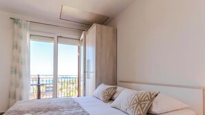 Een hotelkamer met een bed, een nachtkastje, een raam met gordijnen en uitzicht op een balkon.