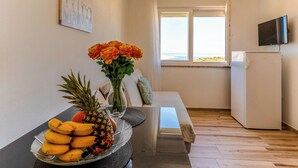 Een eethoek met een tafel gedekt voor twee personen, een schaal fruit, een vaas met bloemen en uitzicht op de omgeving door een raam.