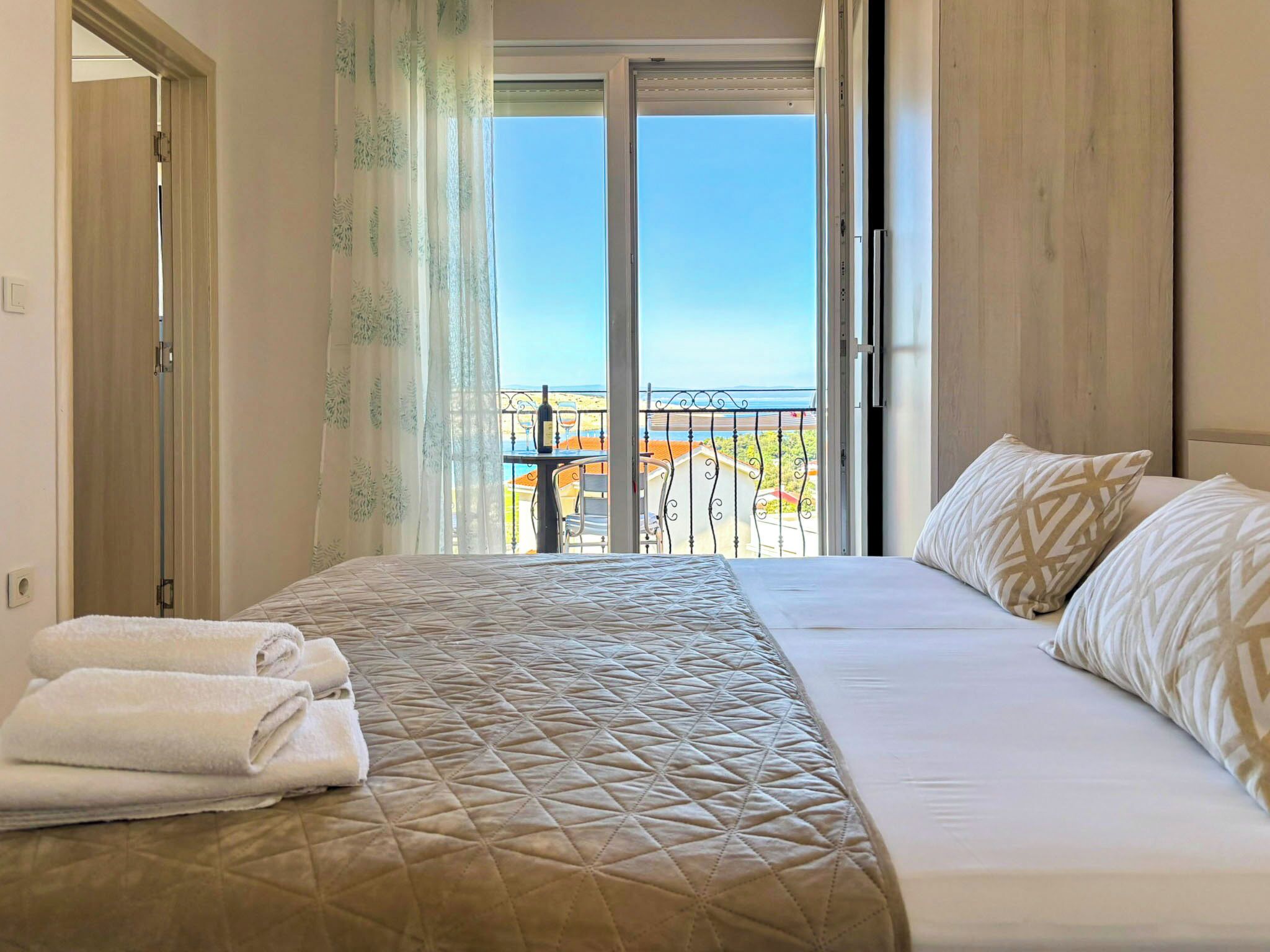 A hotel room with a bed, a balcony with a view, and a door leading to another room.