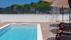 Ein Pool, aus dem Wasser in einen Beckenbereich gefüllt wird, umgeben von Liegestühlen und bewölktem Himmel.
