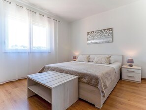 A bedroom with a bed, bedside tables, a nightstand, a window with sheer curtains, and a wall-mounted artwork. - Villa Mare by Interhome (Rab/Lopar)