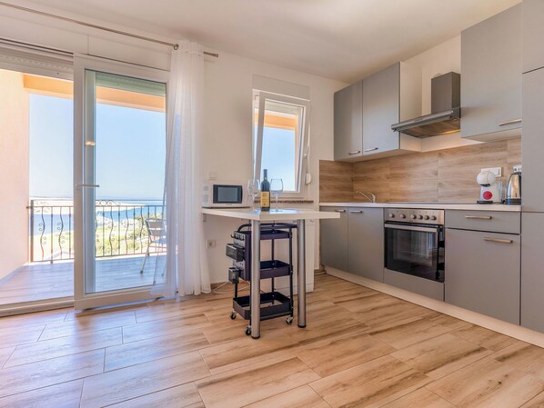 A modern kitchen with a microwave, oven, and coffee maker, a small table with a wine glass, and a view of the sea through a balcony. - Villa Mare by Interhome (Rab/Lopar)