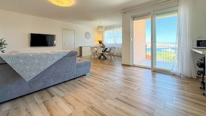 Ein modernes Wohnzimmer mit einer Couch, einem Essbereich mit Stühlen, einem an der Wand befestigten Fernseher und einem Balkon mit Blick.