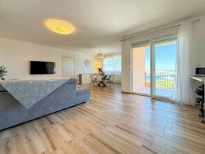 Ein modernes Wohnzimmer mit einer Couch, einem Essbereich mit Stühlen, einem an der Wand befestigten Fernseher und einem Balkon mit Blick.