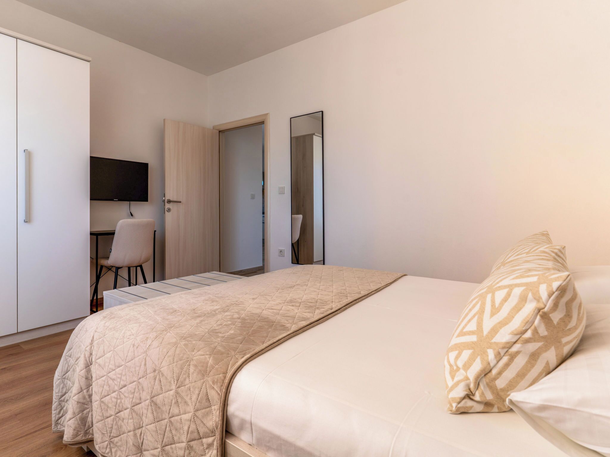 A bedroom with a bed, a desk, a chair, a wardrobe, and a mirror.