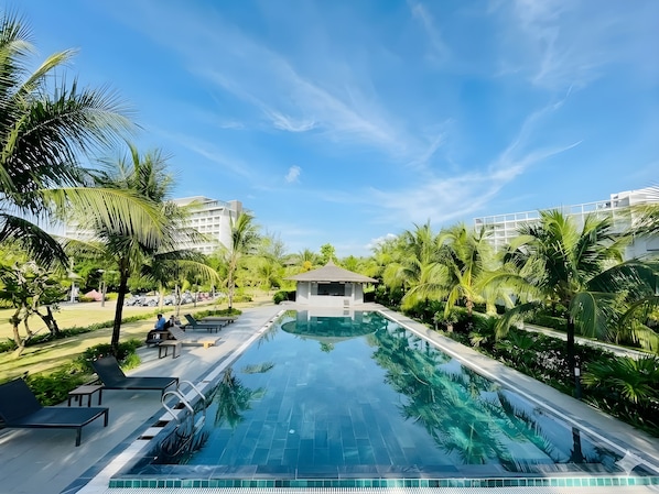 A swimming pool surrounded by palm trees and lounge chairs, with a small pavilion and modern buildings in the background. - V-Luxury Villas Phu Quoc (Phú Quôc)