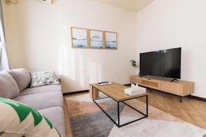 Ein modernes Wohnzimmer mit Sofa, Couchtisch, Fernseher und Kunstwerken an der Wand.