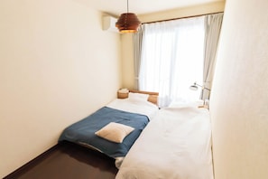 Ein Schlafzimmer mit zwei Betten, einem Nachttisch, einer Lampe und einem Fenster mit Vorhängen.
