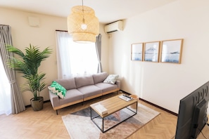 Ein Wohnzimmer mit Sofa, Couchtisch, Zimmerpflanze, einer Pendelleuchte und gerahmten Bildern an der Wand.