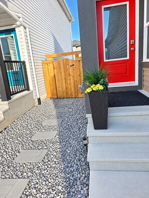 A residential property with a red door, a wooden gate, and a gravel pathway leading to the entrance. - Sleep in Silverstone queen size bed & enjoy our 7-Stage Water filtration System. (Edmonton)