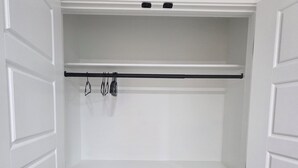 A walk-in closet with white paneled doors, a black rod for hanging items, and a grey wooden floor.