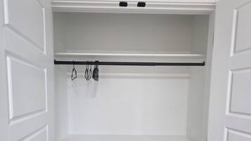 A walk-in closet with white paneled doors, a black rod for hanging items, and a grey wooden floor.