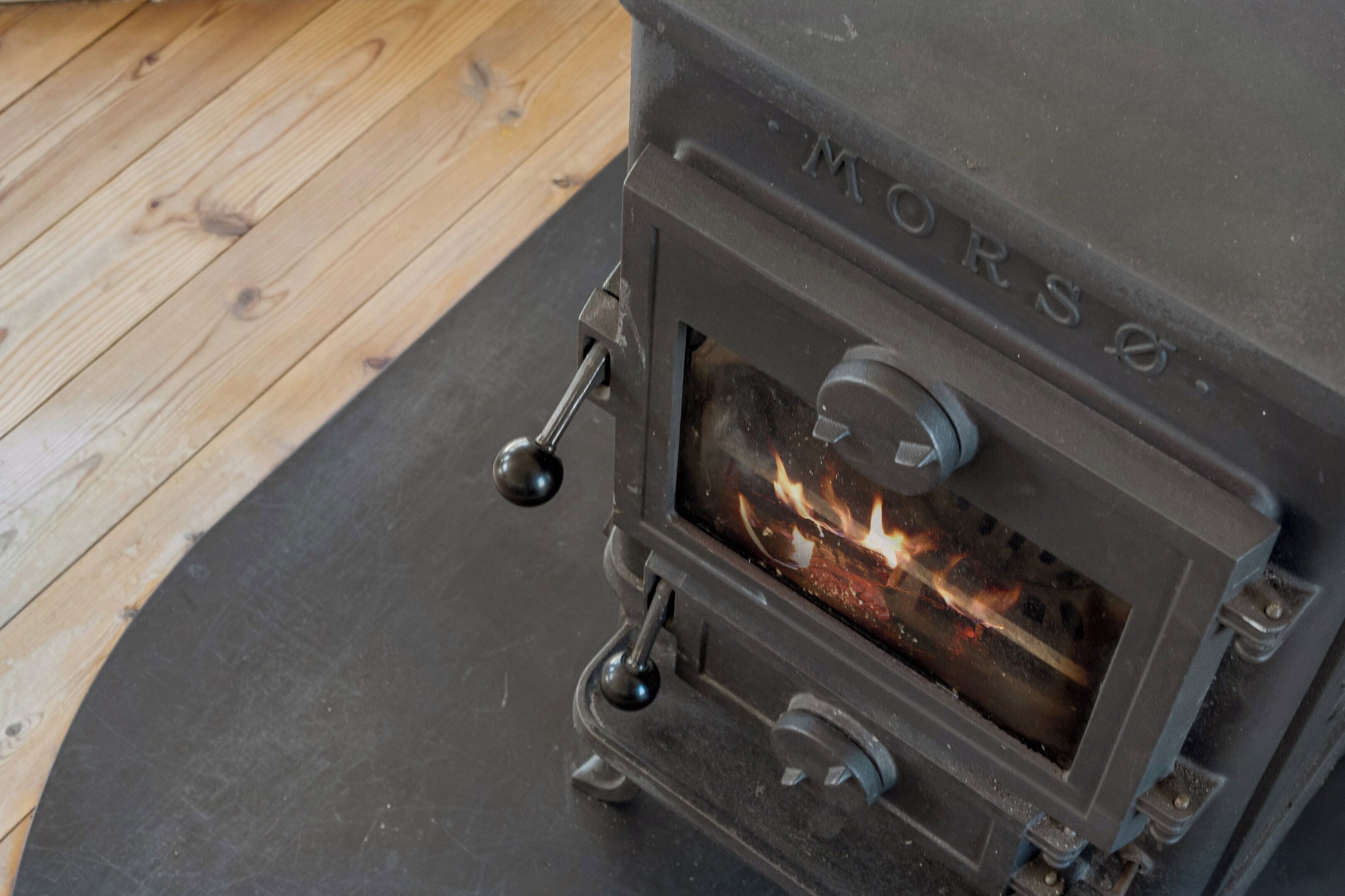 A wood-burning stove with a visible fire, metal handles, and a metal grate.