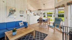 A spacious living area with a blue sofa, wooden coffee table, and a dining table with chairs. - Charming holiday home near the beach (Hejls)