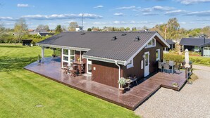 A modern house with a large deck, a covered patio, and a well-maintained lawn. - Charming holiday home near the beach (Hejls)