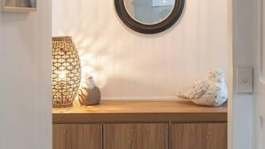 Une console en bois surmontée d’un miroir rond, un luminaire fixé au mur et un vase décoratif.