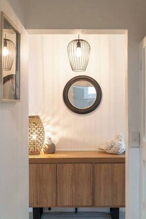 A wooden console table with a round mirror above it, a wall-mounted light fixture, and a decorative vase. - Charming Sans Souci Cottage with Garden & Verandah (Sans Souci)