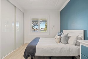 A bedroom with a bed, a window with blinds, a wardrobe, and a blue wall.