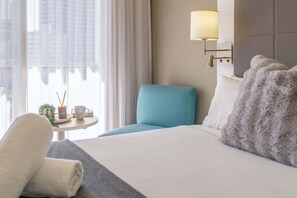 A hotel room with a bed, a blue armchair, a small table with a plant, a lamp, and a window with curtains. - Ocean View Suite 2 Beds Wi-Fi Netflix (Surfers Paradise)
