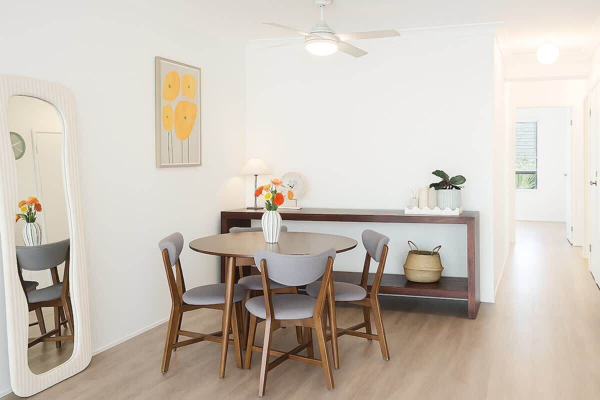 Een eetgedeelte met een ronde tafel, vier stoelen, een plafondventilator, een spiegel en een console tafel met decoratieve objecten.