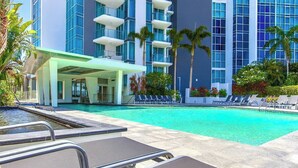 Ein Hotelpoolbereich mit Liegestühlen, einer überdachten Lounge und einem Gebäude mit mehreren Balkonen.