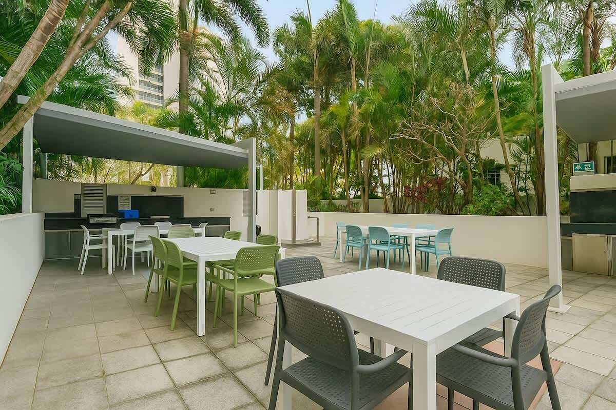 An outdoor patio with tables and chairs, a grill, and lush greenery.